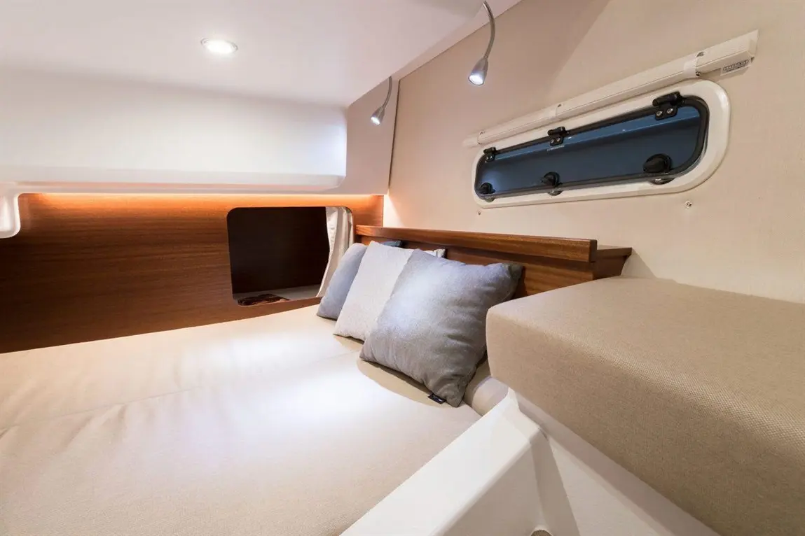 Cozy cabin interior featuring a double bed with grey pillows, soft lighting, and a window for natural light.